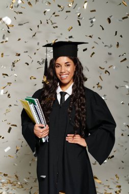 Konfeti üzerine çökerken gecelikli mutlu bir mezun elinde defterler tutuyor..