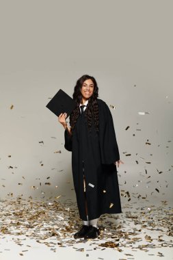 Zarif mezuniyet kıyafetleri içinde genç bir öğrenci düşen konfetilerin arasında kutlama yapıyor..