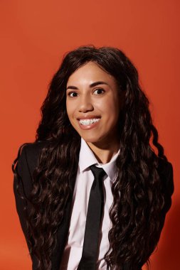 Uzun, dalgalı saçlı neşeli bir öğrenci resmi giyinmiş, neşeli poz verir..