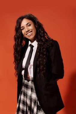 Güzel genç bir kadın, arkasında kalın bir mandalina rengi olan okul üniforması giyerek sıcacık gülümsüyor..