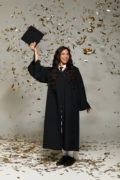 Resmi giyinmiş neşeli bir öğrenci mezuniyeti düşen bir konfetiyle kutluyor..