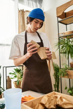 Genç adam, yeşillik ve yaşamla dolu güneşli bir stüdyoda bitki naklediyor..