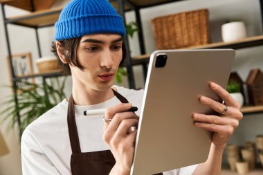 Yakışıklı genç adam, rahat bir stüdyo ortamında tabletle bitki nakletmeye odaklanmış..