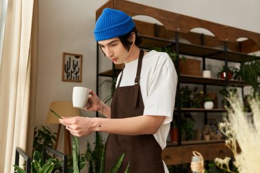 Genç bir adam elinde bir kupa tutarken, çeşitli yemyeşil bitkilerle dikkatlice inceler..