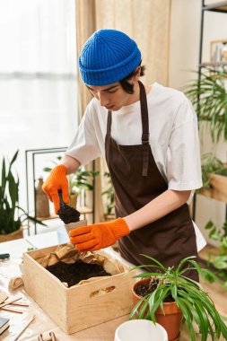 Eldiven takan ve bereli genç adam iyi aydınlatılmış bir stüdyoda toprak ve bitkileri ustalıkla aktarıyor..