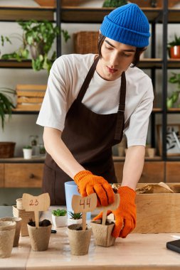 Sıcak kahverengi önlüklü genç bir adam canlı bir stüdyoda ustalıkla küçük bitkileri naklediyor..