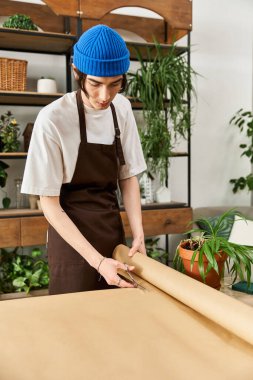 Önlüklü genç adam doğayla çevrili canlı bir stüdyoda bitkileri ustalıkla paketliyor..