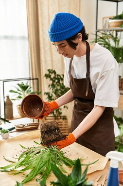 Odaklanmış genç bir adam bitkilerle dolu iyi aydınlatılmış bir stüdyoda dikkatlice yeşillik naklediyor..