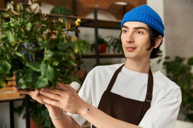 Mavi bereli genç bir adam yeşillik dolu güneşli bir stüdyoda bitki naklediyor..