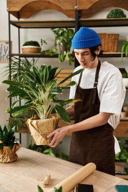 Genç bir adam, bir stüdyoda çeşitli yeşilliklerle çevriliyken yemyeşil bir bitkiyi dikkatlice naklediyor..
