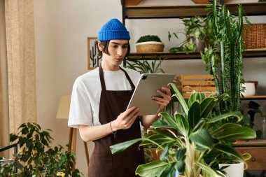 Mavi bereli genç bir adam, parlak bir stüdyoda bitki büyümesini tabletle izliyor..