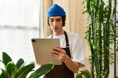 Mavi şapkalı genç bir adam yeşil, parlak, kapalı bir alanda bitki yetiştirme eğilimindedir..