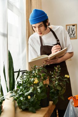 Mavi bereli genç adam sıcak, davetkar bir stüdyoda bitkilerle ilgilenirken notlar alıyor.