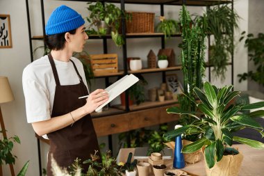 Genç adam kapalı alandaki bitkilere eğilimlidir ve parlak, canlı bir stüdyo ortamında notlar alır..