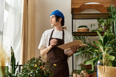 Odaklanmış genç adam dingin bir stüdyo atmosferinin tadını çıkarırken canlı bitkilere eğilimlidir, not alır..