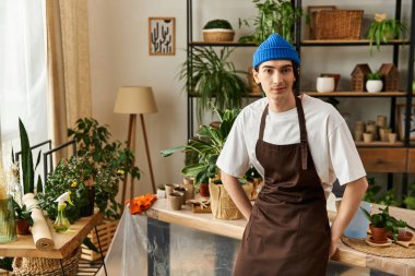 Önlüklü genç adam neşeli bir şekilde canlı bitkilerin arasında poz veriyor..