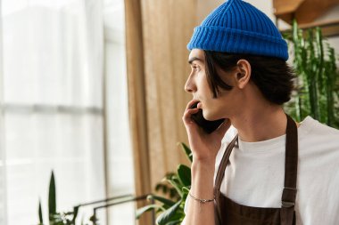 Yakışıklı genç adam, parlak bir stüdyoda çeşitli bitkilerle ilgilenirken telefonda konuşuyor..