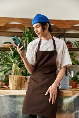 Yakışıklı genç adam, gelişen bitkilerle çevrili canlı bir stüdyoda telefonunu kontrol ediyor..