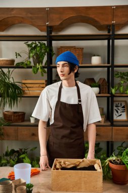 Kahverengi önlüklü genç bir adam stüdyoda saksı bitkileri naklediyor..