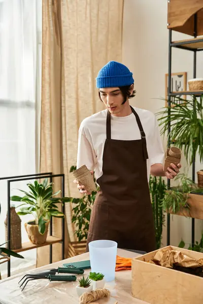 Yakışıklı genç adam iyi aydınlatılmış bir stüdyoda bitkileri yeni saksılara dikkatlice aktarıyor..