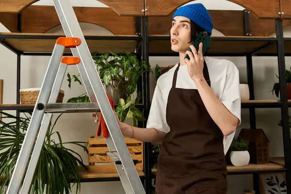 Yakışıklı genç adam modern bir stüdyo ortamında bitkilerle ilgilenirken telefonda konuşuyor..