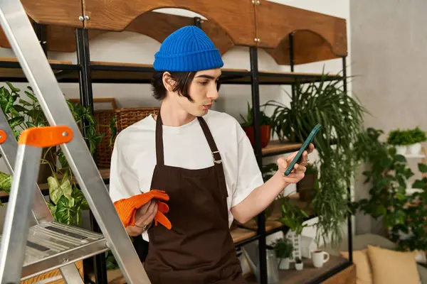 Mavi bereli genç bir adam telefonuna odaklanmış modern bir stüdyoda çiçeklerle ilgileniyor..