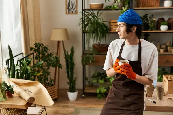 Genç bir adam sıcak, yeşil bir stüdyoda bitki naklederken bardaktan yudumluyor..