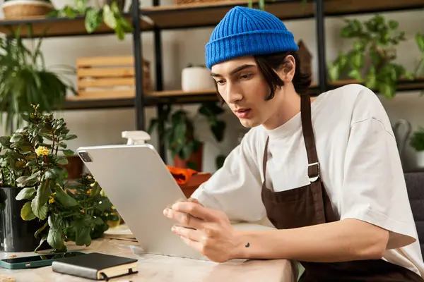 Genç adam yeşillik dolu modern bir stüdyoda bitki yetiştirirken dikkatli bir şekilde bir tablet kullanıyor..