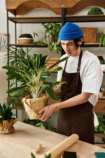 Genç bir adam, bir stüdyoda çeşitli yeşilliklerle çevriliyken yemyeşil bir bitkiyi dikkatlice naklediyor..