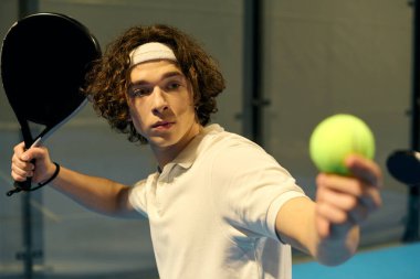 Spor giyim sektöründe genç bir adam Padel 'deki servise hazırlanırken dikkatle odaklanıyor..