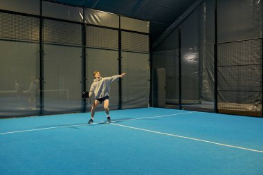 Spor giyim sektöründe genç bir adam kapalı alanda ustalıkla padel oynuyor..