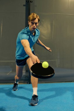 Spor kıyafetlerine odaklanmış genç bir adam sahada ustalıkla Padel oynuyor, atletizmini gösteriyor..