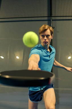 Genç bir sporcu topa uzanırken padel tekniğini gösteriyor..