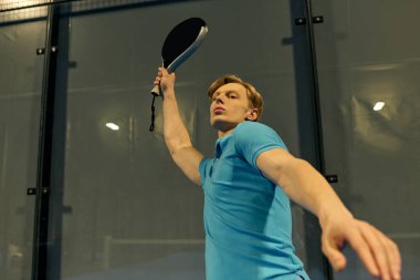 Spor giyim sektöründe genç bir adam sahadaki yoğun bir padel maçında ustalıkla servis yapıyor..