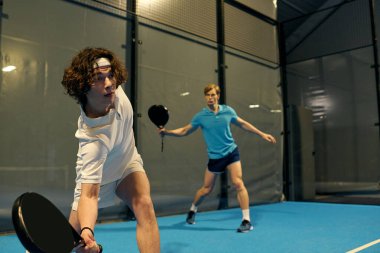 İki genç adam takım çalışması ve becerilerini sergileyerek rekabetçi bir Padel maçına çıkıyorlar..