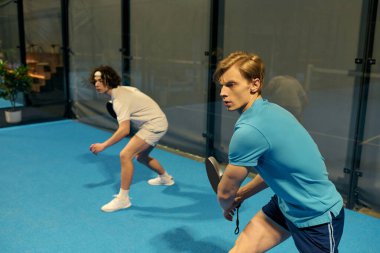 İki genç adam yeteneklerini ve takım çalışmalarını sergileyerek rekabetçi bir Padel oyununa odaklanmış durumdalar..