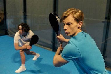 İki genç adam yoğun bir şekilde Padel oyunlarına odaklanmış durumda. Atletizm ve kararlılık sergiliyorlar..