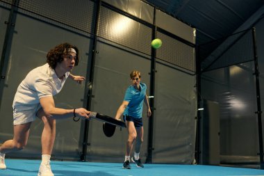 Dinamik genç sporcular yeteneklerini gösterirken kapalı alanda yoğun bir odaklanma ile Padel oynuyorlar..