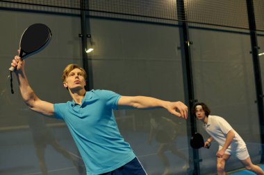 İki genç sporcu yeteneklerini ve takım çalışmalarını sergileyerek enerjik bir Padel maçına çıkıyorlar..