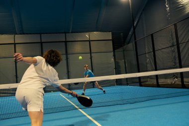 İki genç sporcu, kapalı mekan ışıkları altında heyecan verici bir Padel maçına çıkıyorlar..