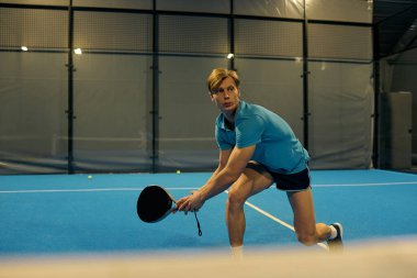 Atletik bir genç adam kapalı alanda oynanan bir maç sırasında topu iade etmeye hazırlanıyor..