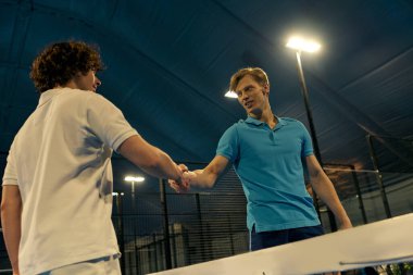 Gergin bir Padel maçından sonra, sportmenlik ve heyecan sergileyen iki genç adam el sıkışıyor..