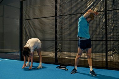 İki genç, mahkeme ağlarının yanında ısınma hareketleri yaparak antrenmana hazırlanıyor..