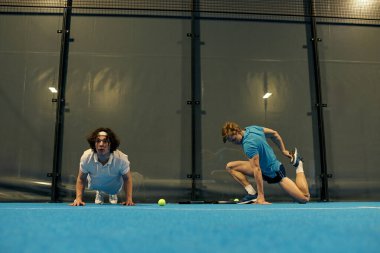 Modern bir mahkeme salonunda Padel oynamadan önce iki genç sporcu yeteneklerini sergiliyor..