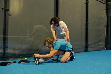 İki genç sporcu, yeteneklerini geliştirmek için parlak mavi bir padel kortunda antrenman yapıyorlar..