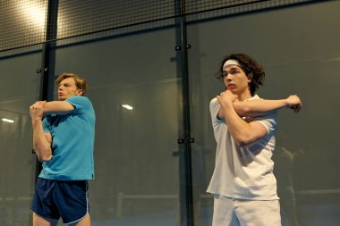 Modern bir spor tesisinde heyecanlı bir maç öncesi iki genç adam esnek bir şekilde ısınıyor..