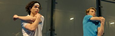 Padel kortunda heyecanlı bir maçtan önce kollarını uzatarak ısınan iki genç adam, afiş.