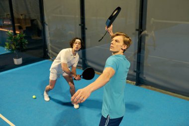 İki genç adam Padel kortunda atletizm göstergesi olarak yoğun bir maç yapıyorlar..