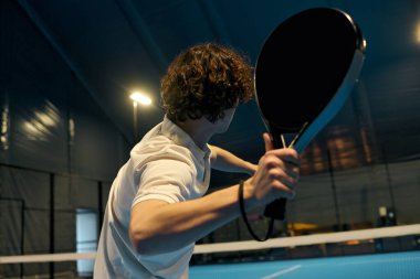 Genç bir adam padel becerilerini canlı bir iç mekanda çalışıyor..
