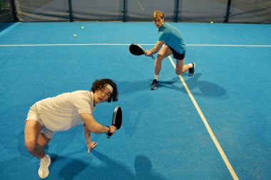 Canlı bir atmosferde Padel oynarken iki genç adam yeteneklerini sergiliyor..